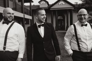Three men in formal attire with suspenders and bowties stand together outdoors.