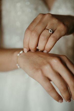 Close-up of hands showing engagement ring and delicate pearl bracelet.
