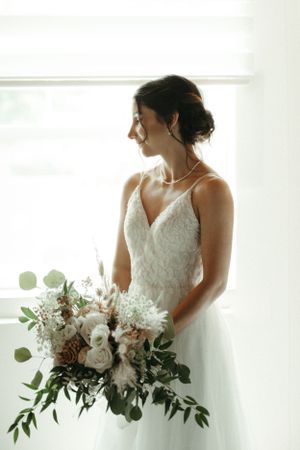 A person in a white lace wedding gown holding a beautiful bouquet of white and green flowers.