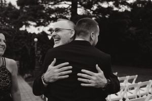Two people share an emotional embrace at an outdoor wedding ceremony.