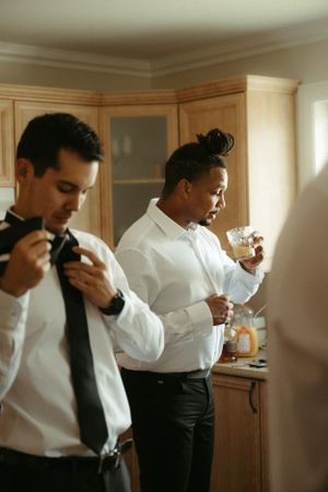Two people in white shirts adjusting their ties while getting ready.
