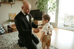 A heartwarming moment as a groom helps a young boy with formal attire in a living room setting.