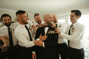 Groomsmen in white shirts and ties share a joyful moment with the groom during wedding preparations.