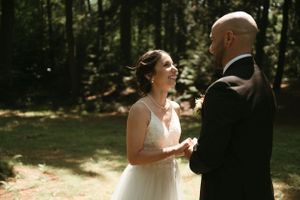 A bride and groom share an intimate moment in a sunlit forest clearing during their wedding.