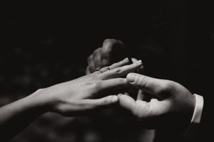 Photo en noir et blanc montrant deux mains échangeant des bagues dans un moment de cérémonie de mariage intime.