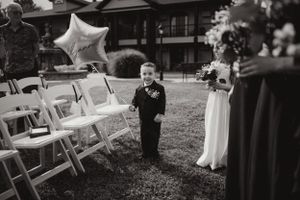 A young ring bearer walks down the aisle at an outdoor wedding ceremony.