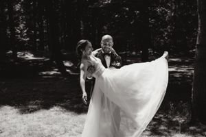 Une photographie en noir et blanc d'un couple en tenue de mariage dansant joyeusement ensemble dans un cadre extérieur boisé. Vive la nature