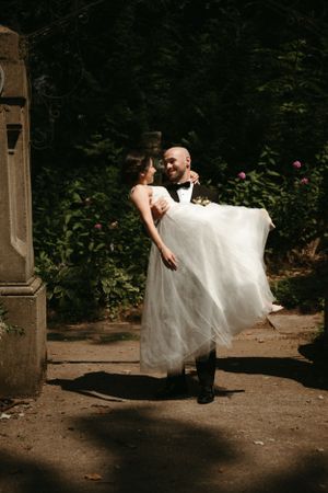 A romantic dip pose between newlyweds near a stone pillar in a garden setting.