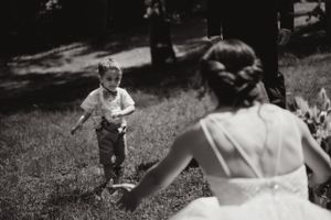 Photographie vintage en noir et blanc montrant un enfant courant sur une pelouse vers quelqu'un en robe de mariage.