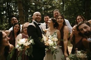 Wedding party gathers for fun candid group photo in forest.