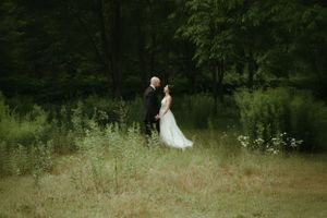 Couple poses in dreamy meadow setting surrounded by tall grass and trees.