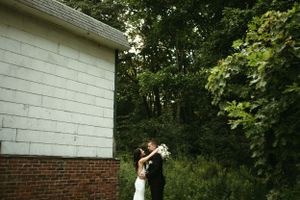 A romantic moment between newlyweds embracing beside a white building with trees in the background.