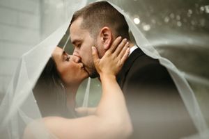 An intimate close-up of a couple kissing beneath a sheer wedding veil.