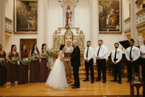 A wedding ceremony takes place in an ornate church with bridesmaids in brown dresses.