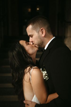 Romantic couple share an intimate kiss in a dimly lit setting during their wedding celebration.