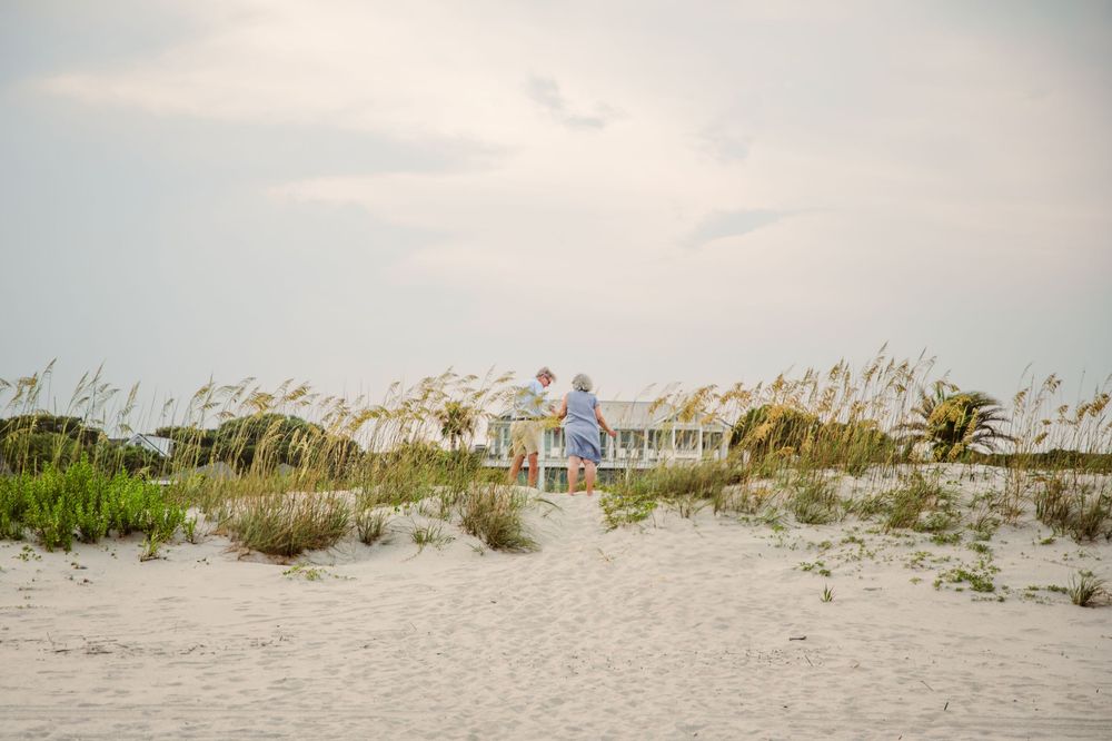 A coastal beach house nestled behind sand dunes and sea oats along a serene shoreline at dusk.