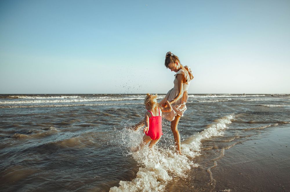People playing and splashing in shallow ocean waves at the beach during a sunny day.
