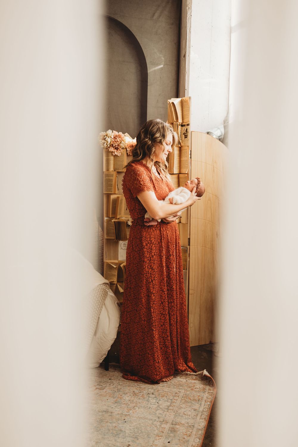 Figure in a flowing rust-colored maxi dress stands near wooden shelves in warm natural light.