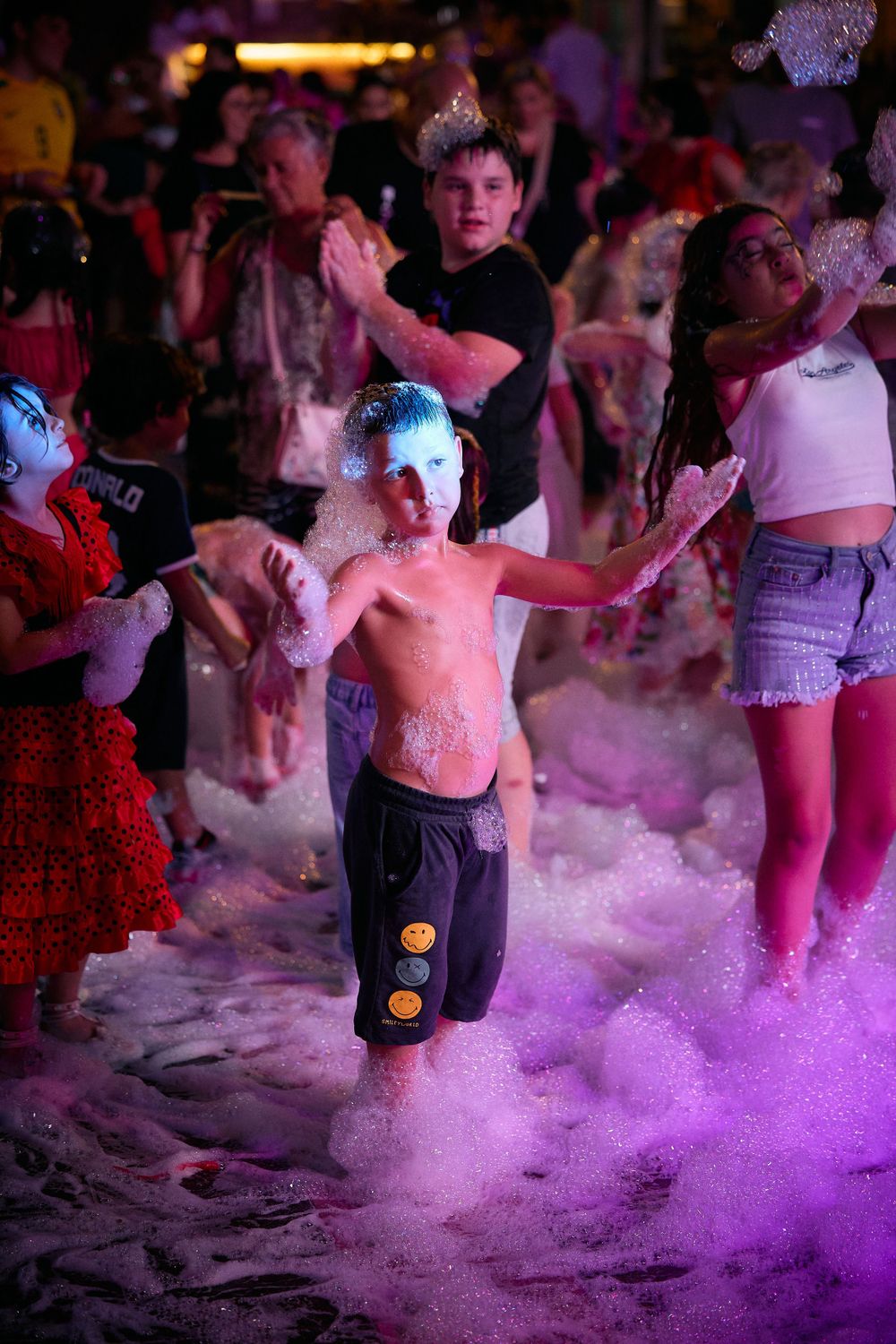Partygoers dancing in purple foam at a nighttime outdoor celebration.