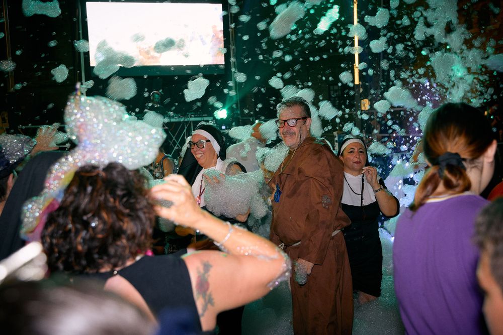 Crowd enjoying a foam party with bubbles in a dark venue with colorful lighting.