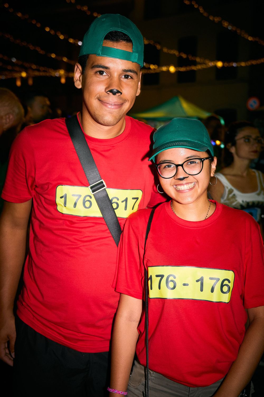 Two people wearing matching red t-shirts with number bibs at a nighttime event.