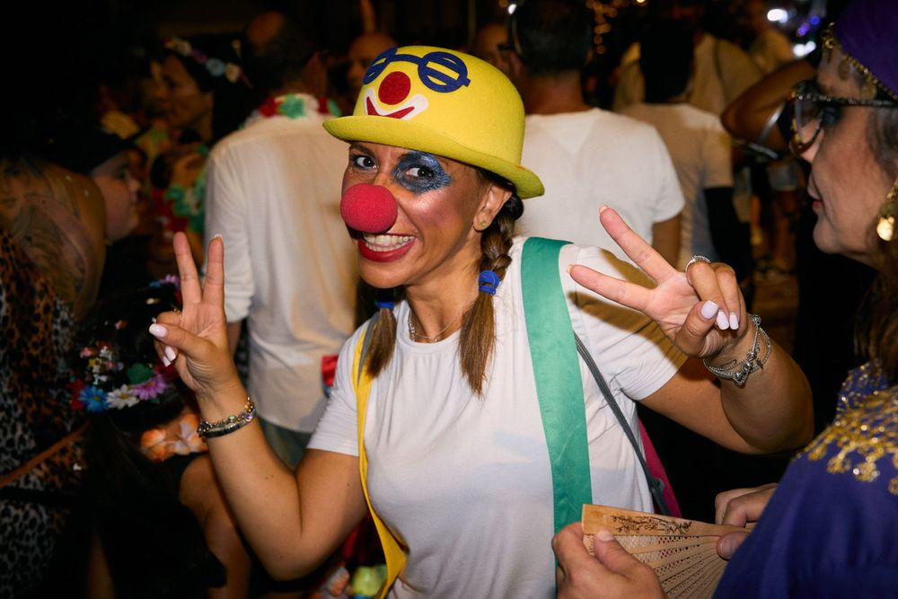 Person in a yellow hat and white shirt making peace signs at a costume party.