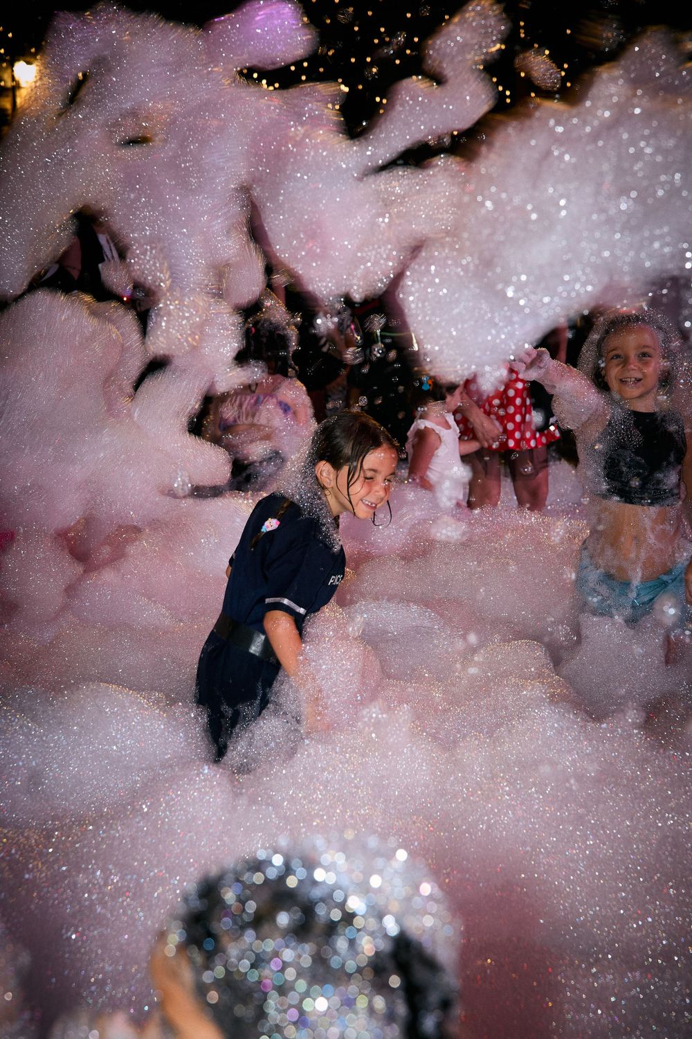 Crowd surrounded by pink foam and glitter at a nighttime party.