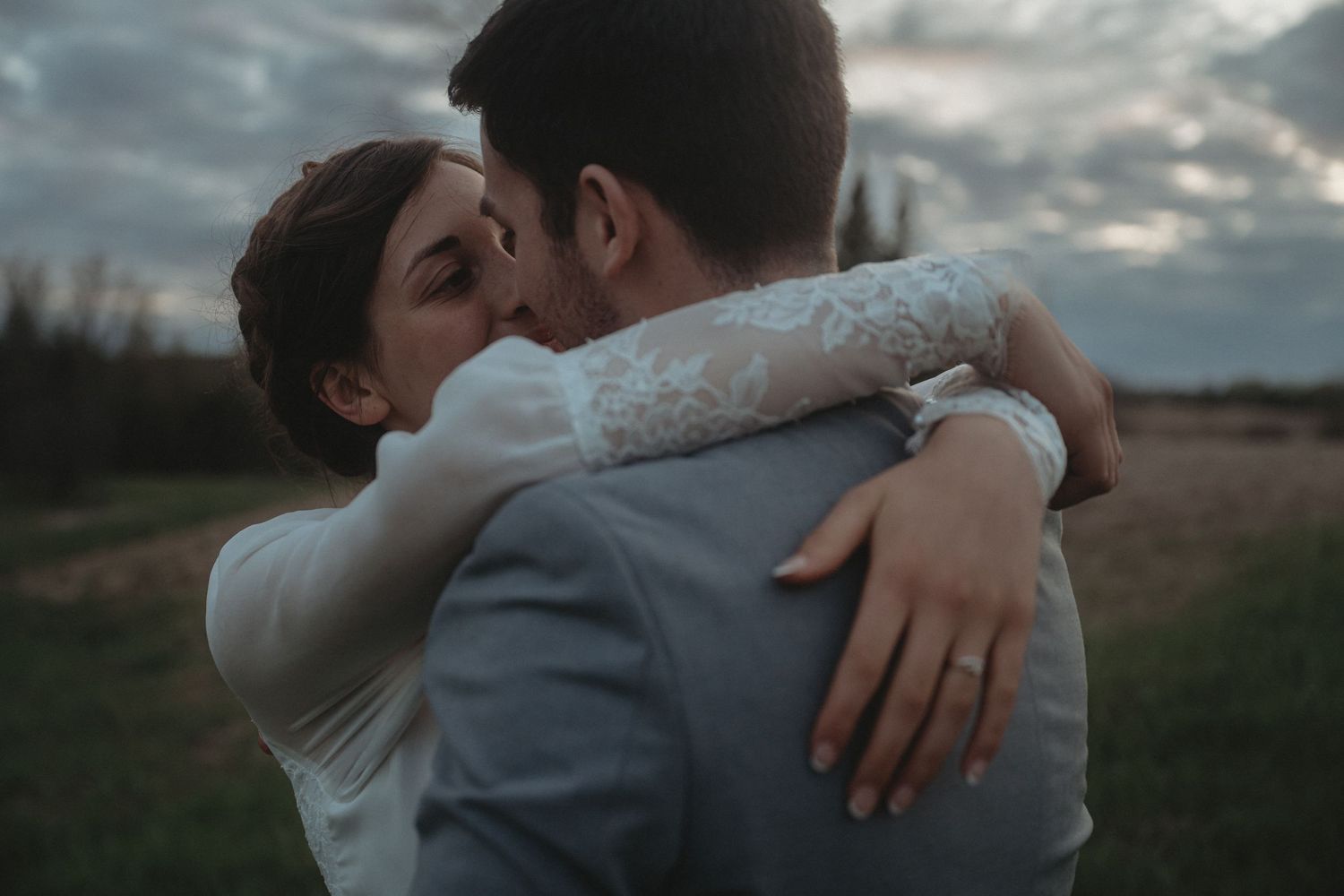 An intimate moment between newlyweds sharing an embrace against a moody sky.