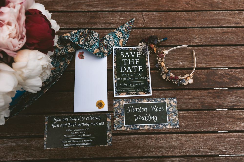 Wedding invitation suite with floral details and rings on rustic wooden background.