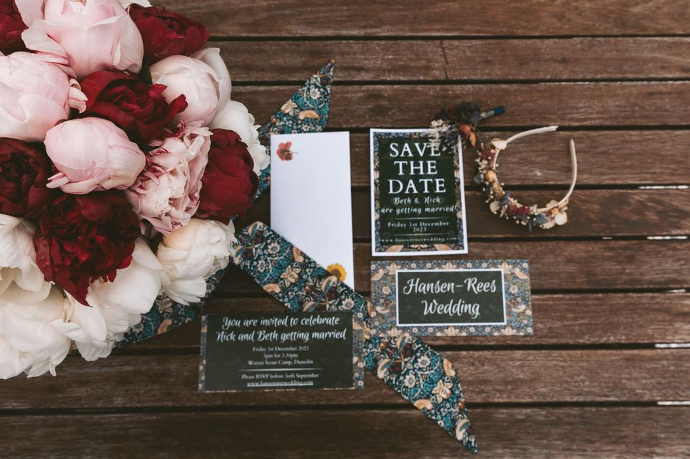 Wedding invitation suite with pink peonies and blue butterflies on rustic wooden background.
