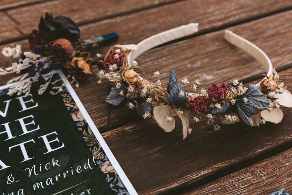 Dried floral crown and wedding invitation on wooden surface.