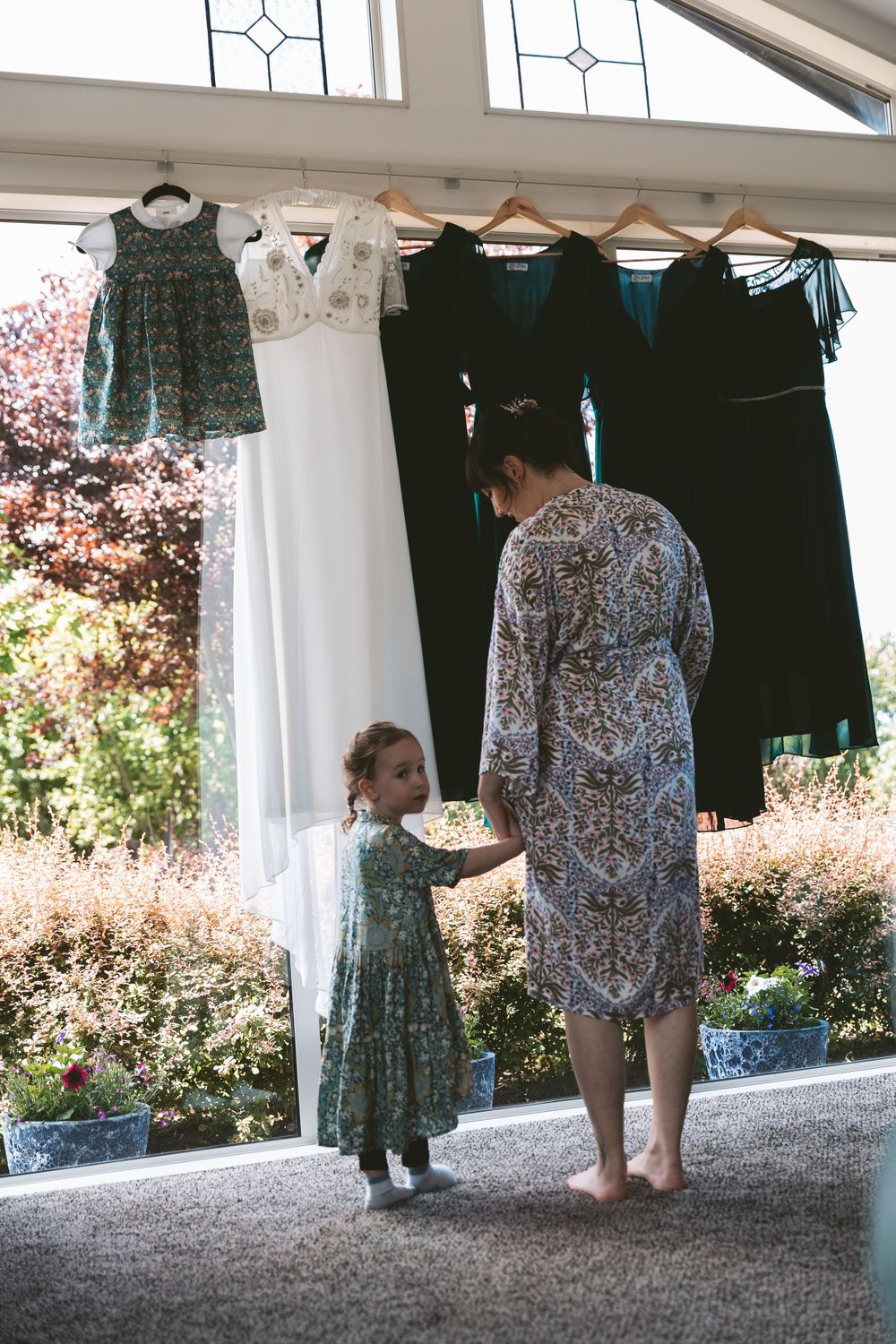 Wedding dresses and formal attire hanging by window with morning light.