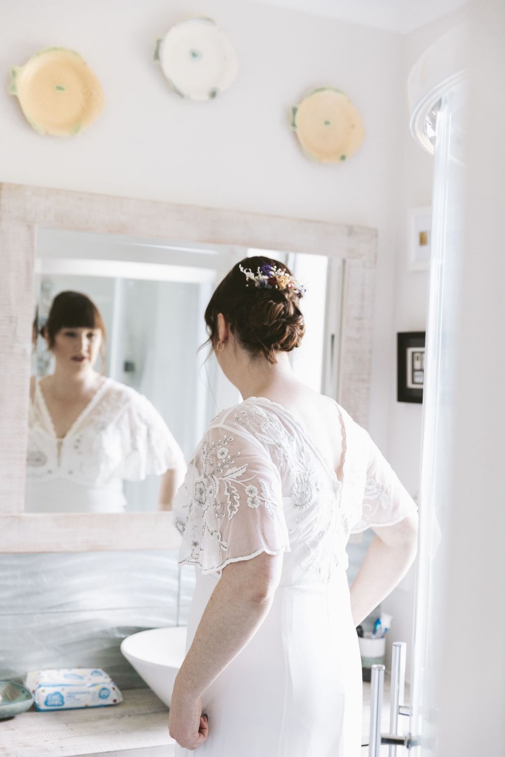 Bride admiring wedding dress reflection in bathroom mirror.