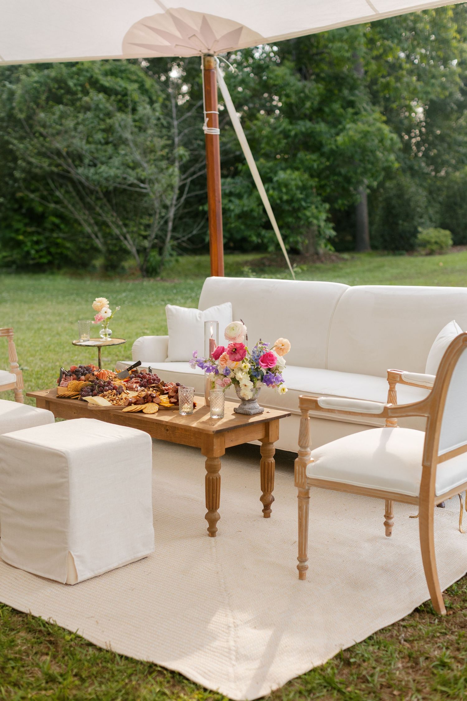 Elegant outdoor lounge area with white furniture and wooden serving tray under umbrella.
