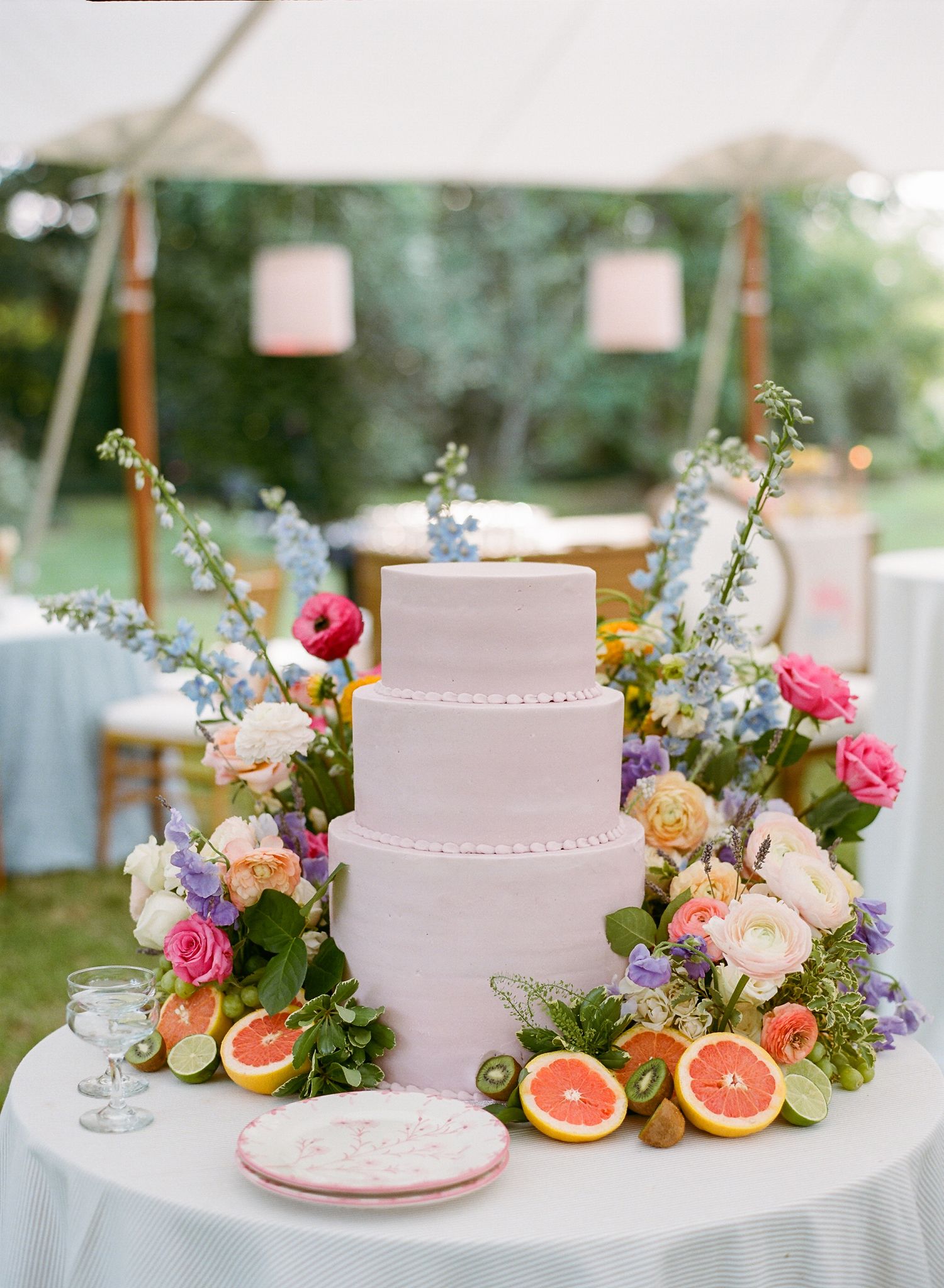 Three-tiered white wedding cake decorated with colorful flowers and citrus fruit slices.