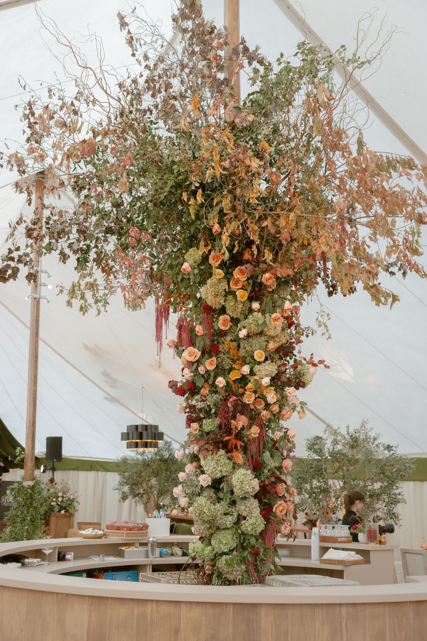 Large floral installation with cascading greenery and autumn-colored blooms decorates a reception tent pole.