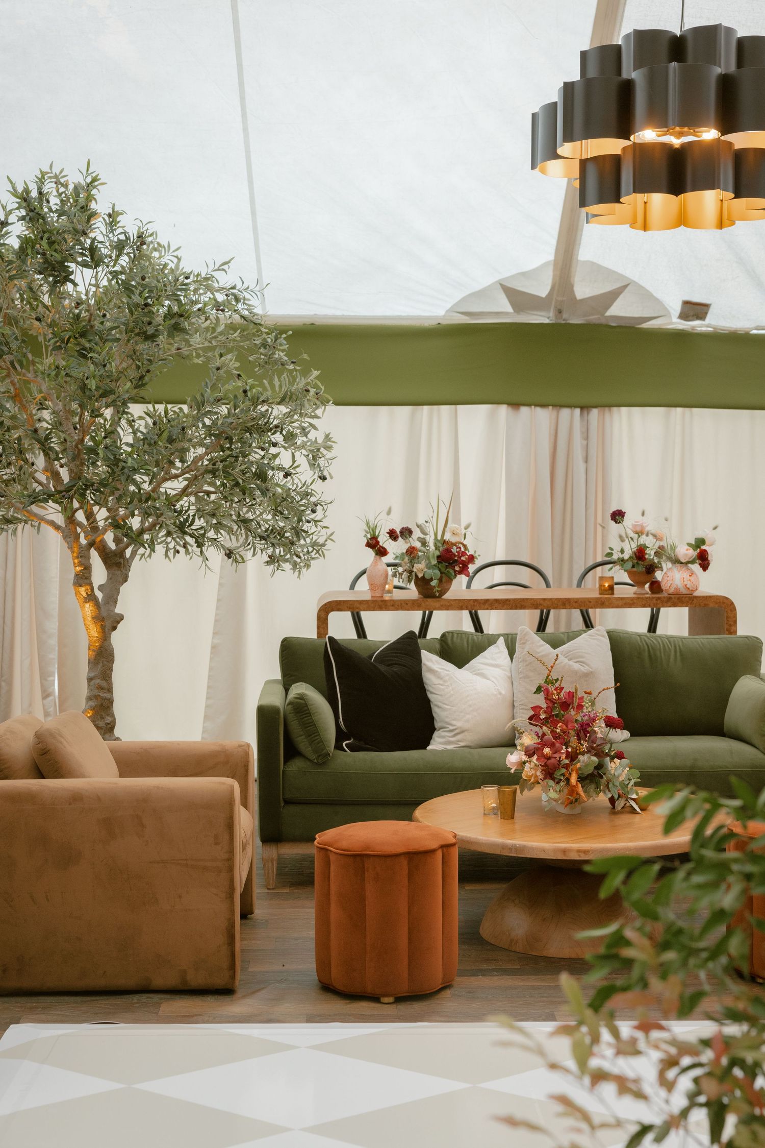 Modern lounge setup with green velvet sofa, tan accent chair, and wooden tables under contemporary pendant lighting.
