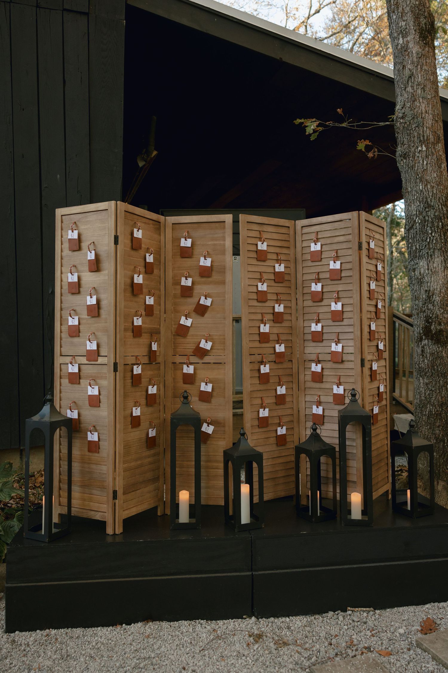 Wooden folding screen with numbered card holders and black lanterns arranged as a decorative seating chart display.