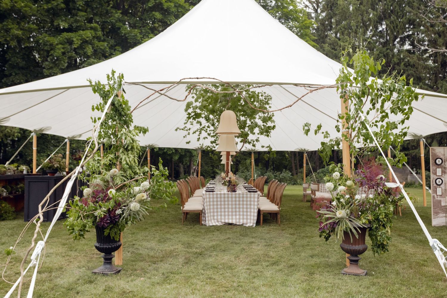 Large white wedding tent decorated with potted plants and greenery on a manicured lawn.