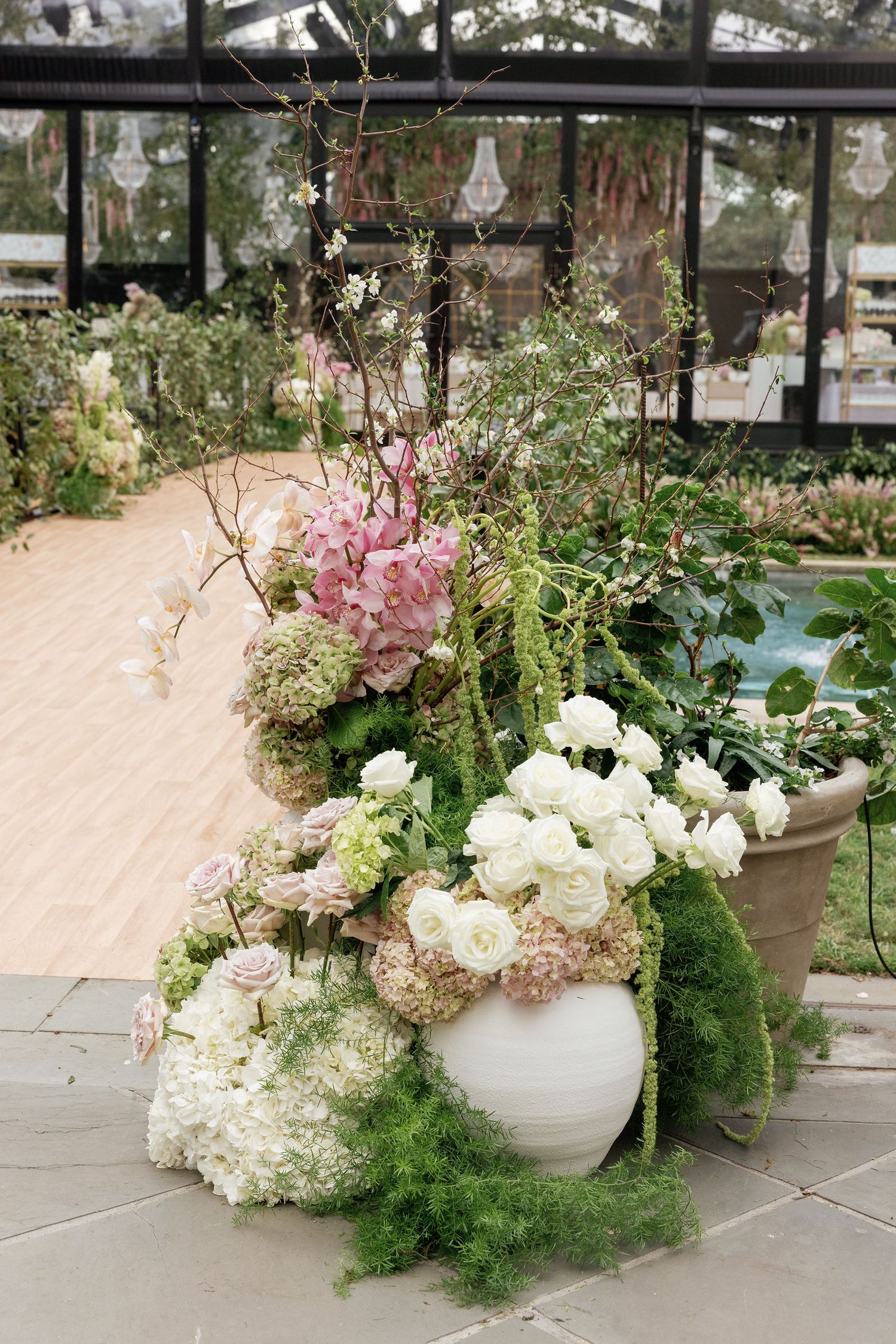 A beautiful floral arrangement of white hydrangeas and pink blossoms in white vases against a greenhouse backdrop.
