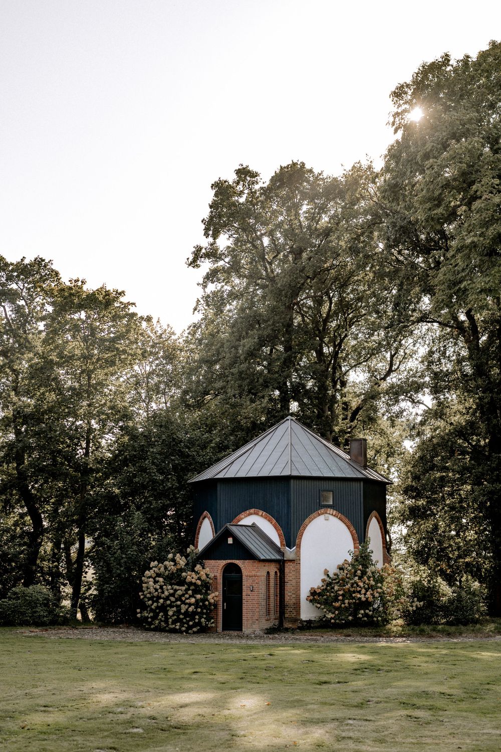 Charming octagonal chapel building surrounded by lush trees and gardens.