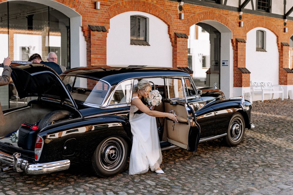 Wedding scene with classic vintage black car parked in front of brick archways.