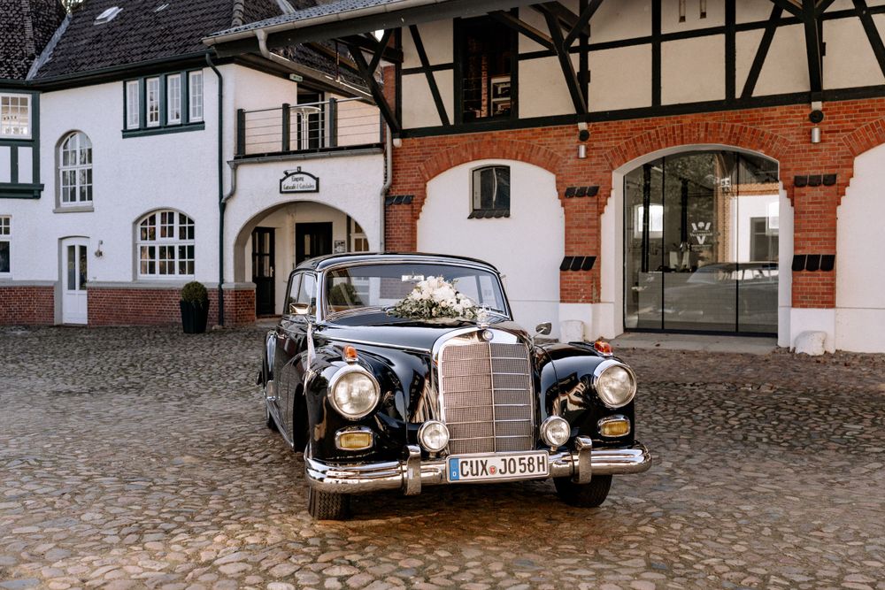 Vintage black Mercedes sedan parked in front of historic European buildings with timber frame architecture.