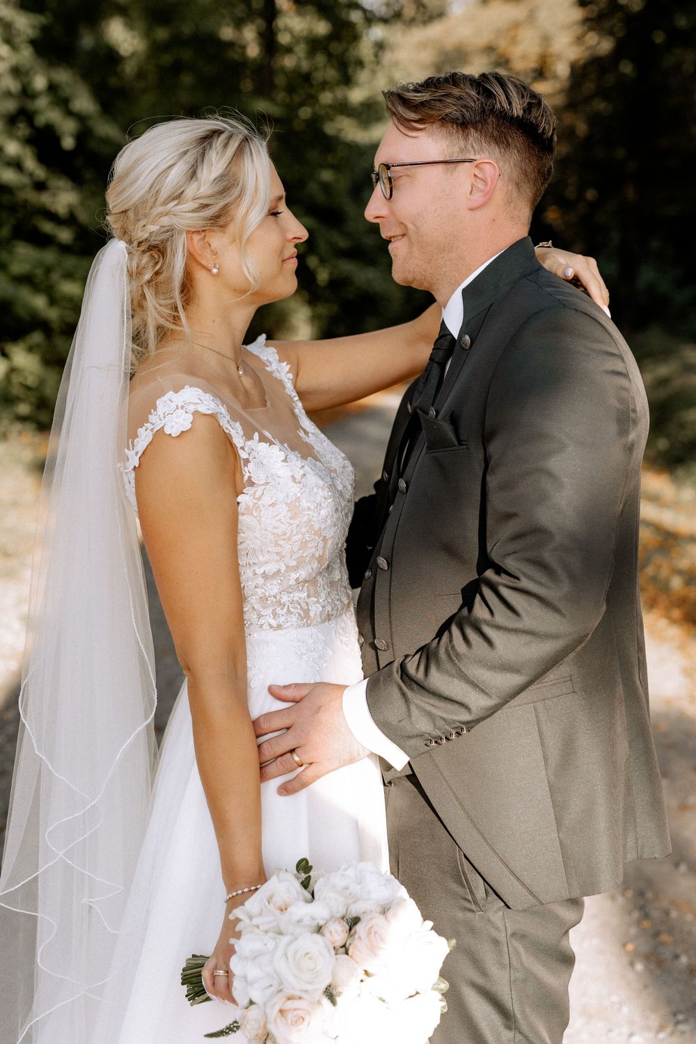 A romantic wedding couple embracing outdoors in sunlit natural setting.