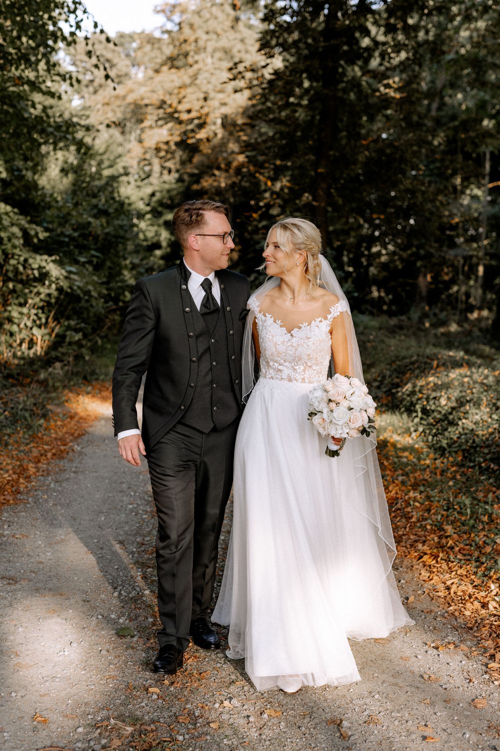 Newlyweds walking together on an autumn forest path with golden foliage.