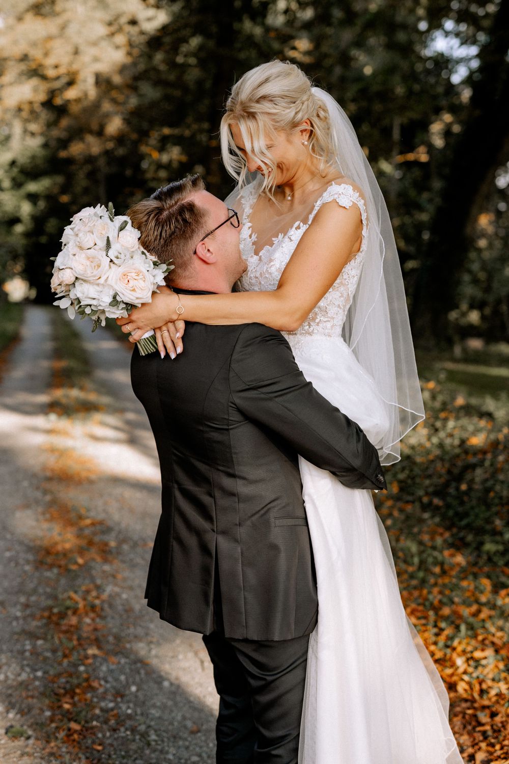 Groom lifts bride in white dress during romantic outdoor wedding photoshoot.