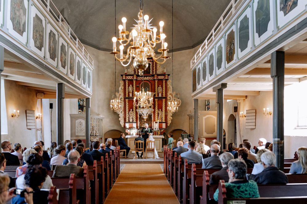 Interior view of ornate church with a grand chandelier and wooden pews filled with people during a religious service.