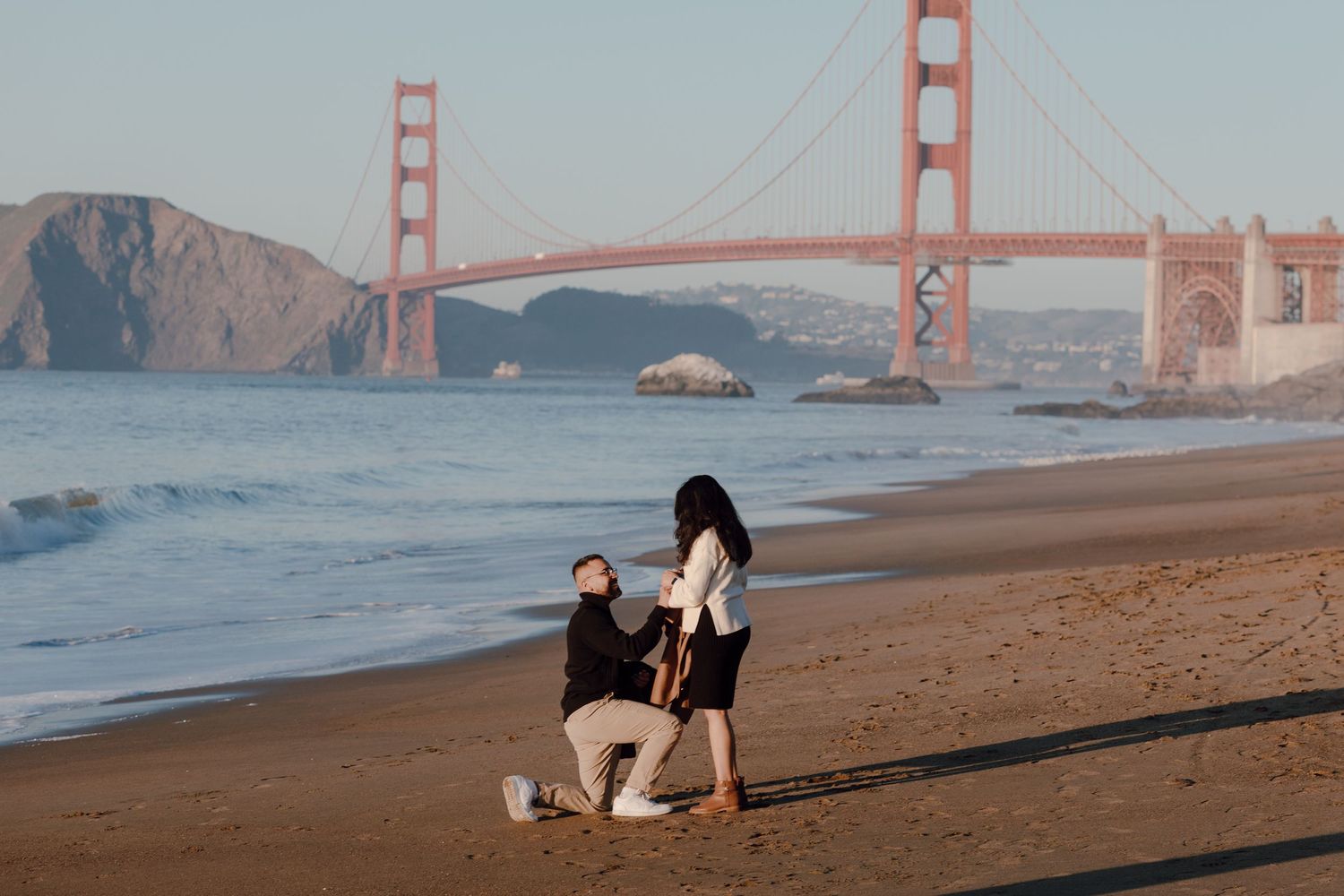 Beach proposal scene with the iconic Golden Gate Bridge in the background during sunset.