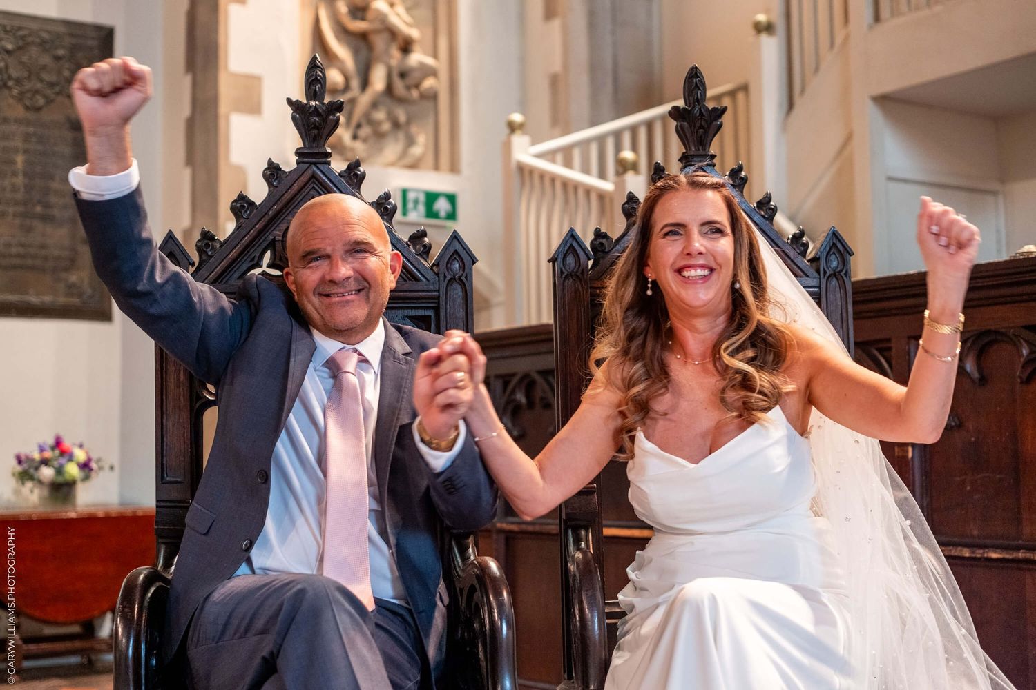A joyful newlywed couple celebrates with raised arms while exiting their wedding ceremony in a church.