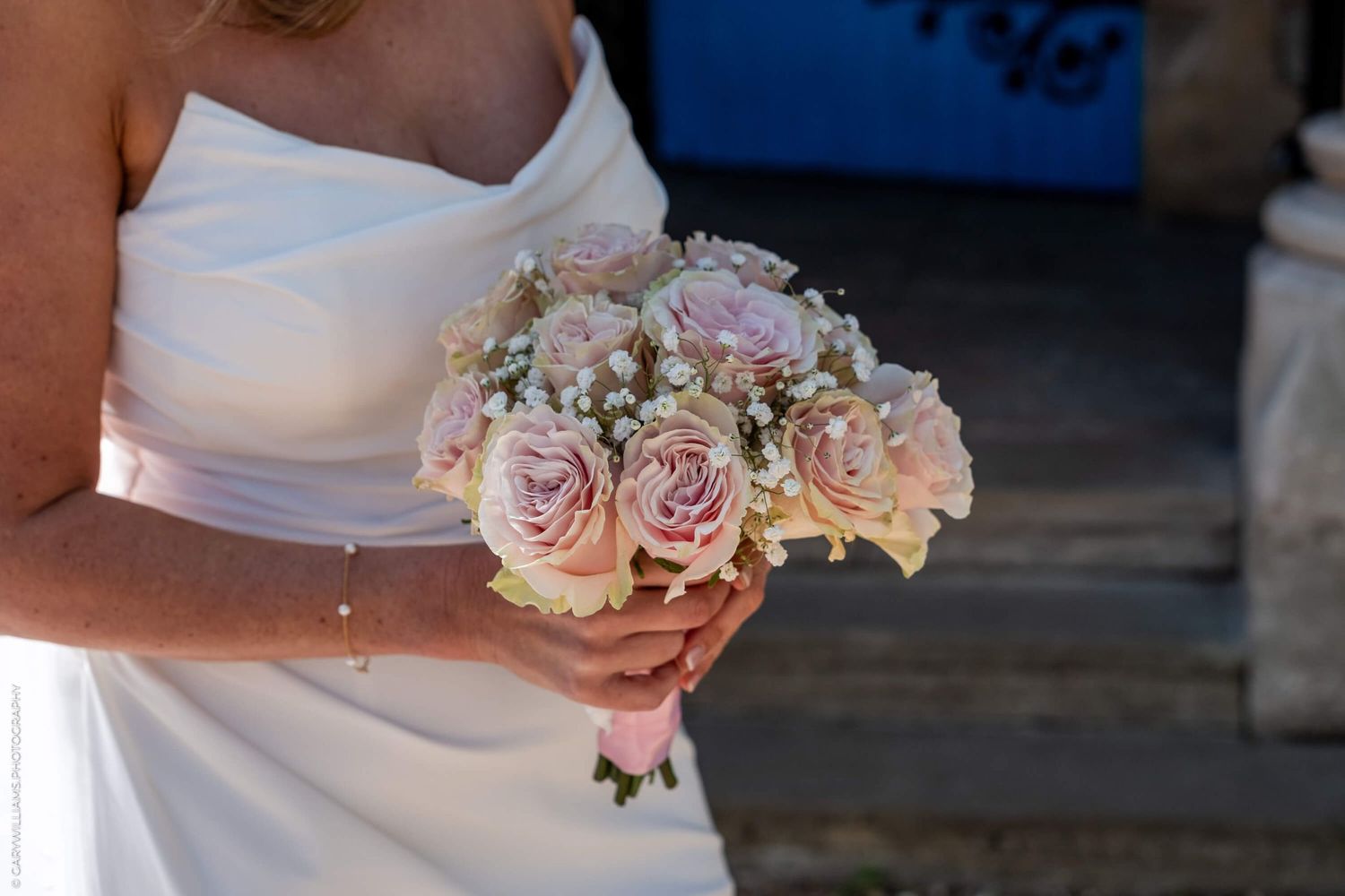 A delicate pink and white rose wedding bouquet held against a white dress.